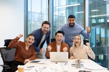 Çeşitli bir ekip, modern ofis ortamında başarı ve neşe ifade eden başarılı bir projeyi kutluyor..
