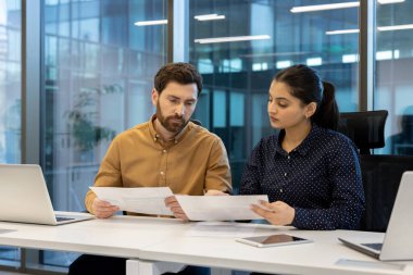 Çeşitli meslektaşlardan oluşan bir ekip modern ofis ortamında işbirliği yapıyor, belgeleri inceliyor ve çalışmaları sırasında teknolojiyi kullanıyorlar..