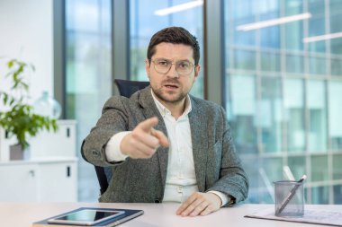 Kızgın genç iş adamının portresi çevrimiçi bir toplantı düzenliyor, agresif bir şekilde konuşuyor ve suçlayıcı bir parmağı kameraya doğrultuyor..