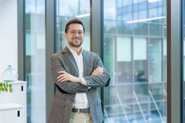 Bir şirket ve şirketin kurucusu ve sahibi, gülümseyen genç bir adam, bir ofis binasının lobisinde duruyor, kolları göğsünde ve kendinden emin bir şekilde kameraya bakıyor..