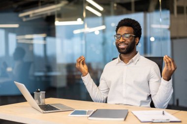 Bir Afro-Amerikalı ofis masasında meditasyon yapıyor, farkındalığı ve iş-yaşam dengesini teşvik ediyor..