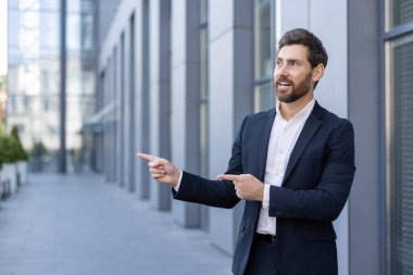 Takım elbiseli bir işadamı, modern bir ofis binasına karşı duran bir tarafı işaret ediyor..