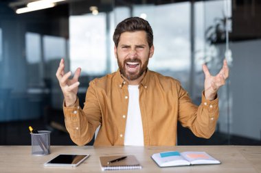 Profesyonel ortamda hayal kırıklığına uğramış bir adam, öfke ve kızgınlığını ifade ediyor, elleriyle işaret ediyor ve kameraya bağırıyor..