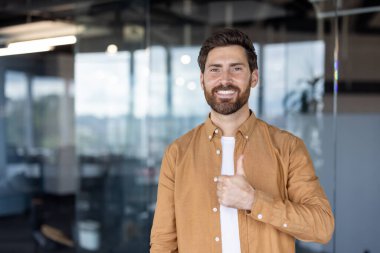 Gülümseyen, sakallı bir adam modern ofis ortamında olumlu ve onaylı bir şekilde onay veriyor..