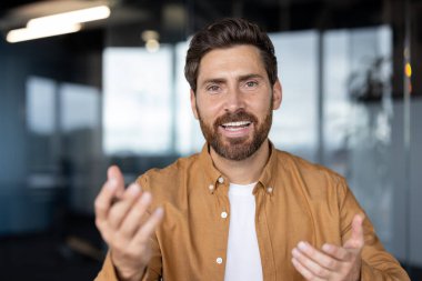 Ofis ortamında sakallı gülümseyen bir adam, muhtemelen bir video görüşmesi veya sunum sırasında..