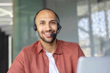 Kulaklık takan gülümseyen bir adam, muhtemelen bir müşteri hizmetleri temsilcisi, doğrudan kameraya bakıyor..