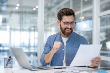 Gözlüklü bir adam gülümsüyor ve elinde bir gazete tutuyor, sanki ofiste başarılı olmuş gibi..