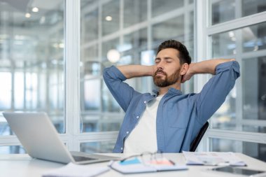 Rahat bir iş adamı masasında oturur, ellerini başının arkasına koyup ara verir. Ofisinde..