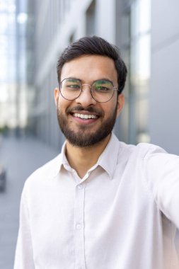Telefon kamerası görüntüsü, iş adamı kameraya bakıyor, iş arkadaşlarıyla konuşuyor memnun bir şekilde gülümsüyor, tişörtlü bir adam ofis binasının dışında yürüyor.