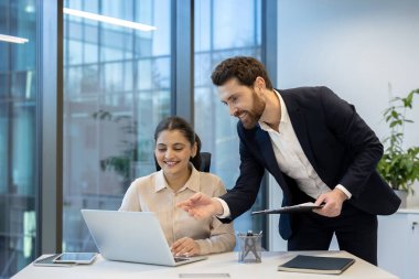 Çeşitli bir ekip, modern bir ofiste birlikte çalışarak bir dizüstü bilgisayar üzerinde çalışırlar. Sahnede profesyonellik ve takım çalışması belirgin.