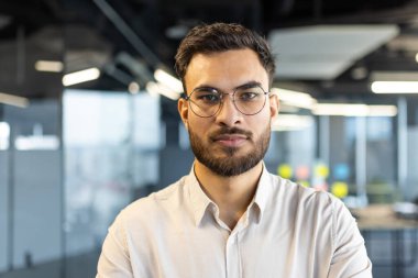Ofis ortamında gözlüklü odaklanmış bir iş adamı. Fotoğraf kendine güvenen ve ulaşılabilir bir bireyi vurguluyor..