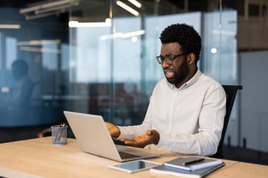 Çağdaş bir ofis ortamında dizüstü bilgisayarla otururken hayal kırıklığını ifade eden profesyonel bir adam. Görüntü, yüksek teknoloji ortamında işyeri stresi ve zorlukları aktarıyor.