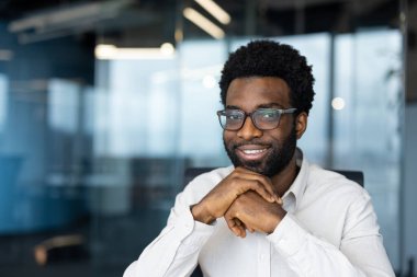 Modern bir ofiste oturan profesyonel bir birey, kendine güven ve pozitiflik yayıyor. İş dünyasının profesyonelliğini, kariyer başarısını veya iş ortamlarını göstermek için ideal görüntü.