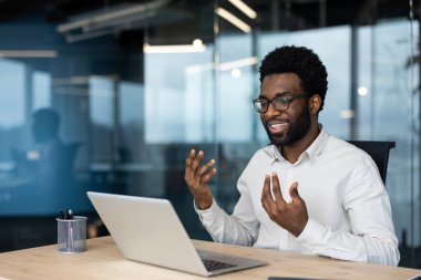 Modern bir ofiste oturan neşeli bir profesyonel, aktif olarak online bir toplantıda dizüstü bilgisayar kullanıyor, çağdaş bir iş ortamında iletişim ve teknolojiyi vurguluyor..