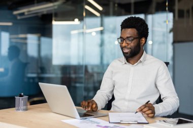 Çağdaş bir ofiste dizüstü bilgisayarda çalışan odaklanmış bir birey. Çevre verimliliği, profesyonelliği ve biraz işbirliği içeren modern bir çalışma ortamını öneriyor..