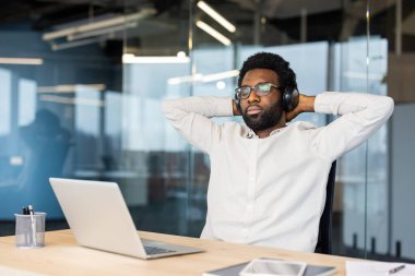 Bir profesyonel, açık dizüstü bilgisayarlı bir masaya oturmuş kulaklık takarak rahatlamanın, iş temaları, rahatlama ve üretkenlik temalarını öne sürerek rahatlamanın keyfini çıkarıyor..