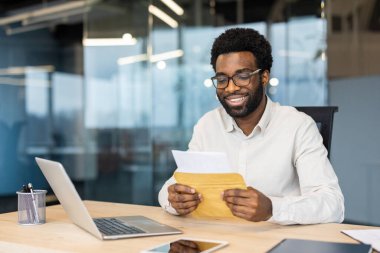 Modern ofiste çalışan bir iş adamı, masasında dizüstü bilgisayarla otururken belgeleri okuyor..
