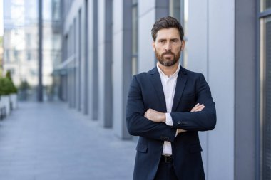 Takım elbise giyen iddialı bir işadamı şehir ortamında güvenle poz verir. Görüntü, çağdaş bir iş ortamında profesyonellik, güven ve liderlik taşıyor..