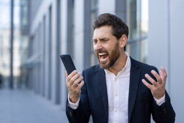 Takım elbiseli sıkıntılı bir işadamı, iş günü modern ofisin dışındaki akıllı telefonuna olan kızgınlığını dışa vuruyor. Bir şehir stresi ve iletişim bozukluğu anı yakalıyor.