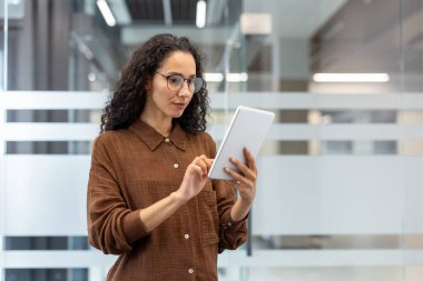Kadın, parlak, çağdaş bir ofis ortamında, profesyonelliği ve teknolojiyi somutlaştıran bir tablet cihazı tutuyor ve kullanıyor..