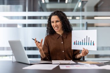 Bir iş adamı, kurumsal ofis ortamında yapılan bir toplantıda performans grafiklerini analiz ederken hayal kırıklığını ifade eder..