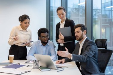 Çeşitli profesyonellerden oluşan bir grup, bir ofis masasında iş görüşmeleri yapıyor, aktif olarak ortak görevlerine odaklanıyorlar..