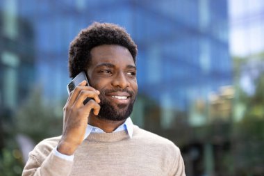 Akıllı telefondan konuşan kendine güvenen bir adam, açık şehir ortamında pozitif ve profesyonel bir tavır sergiliyor..