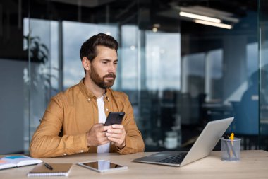 Şık bir ofiste odaklanmış profesyonel görevler için akıllı telefon ve dizüstü bilgisayar kullanır.