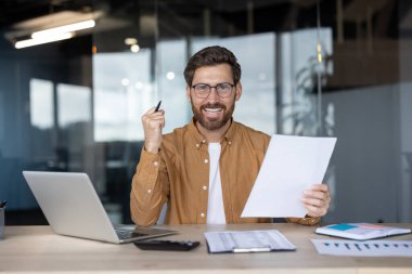 Ofis ayarları. Kendine güvenen bir çalışanın gülümseyerek belgeleri incelemesi.
