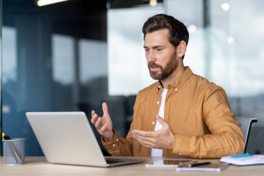 Odaklanmış bir adam iş yerinde dizüstü bilgisayarla online bir tartışmaya girer. Kurulum, toplantı sırasında net ve etkili iletişim sağlayan profesyonel bir atmosfere sahip çağdaş bir ofis..