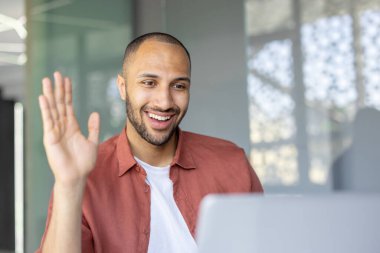 Sanal bir toplantıya katılan dost canlısı profesyonel, bir dalga ve gülümsemeyle pozitif enerjiyi ifade ediyor..