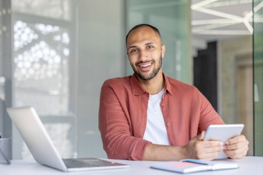 Çağdaş bir mesleki ortamda tablet ve dizüstü bilgisayarla çalışan gülen bir birey üretkenlik ve pozitifliği iletir.
