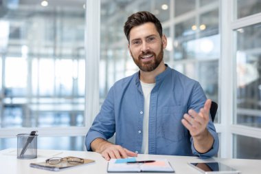 Parlak bir ofis ortamında oturan kendine güvenen bir adam, nişanlanırken el kol hareketi yapıyor..