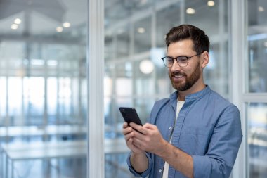 Parlak, modern bir çalışma alanında telefonunu kullanarak gülümseyen bir profesyonel..