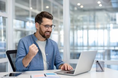 Adam kendini başarılı hissediyor ve bilgisayar kullanırken profesyonel bir çalışma alanında gülümsüyor. Bir iş veya iş ortamında başarı, başarı ve pozitifliği temsil eder.