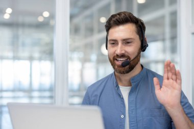 Kulaklık takan neşeli bir adam modern ofis ortamından gelen bir video çağrısına katılıyor..