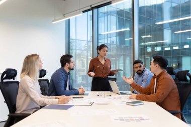Profesyoneller, geniş pencereli, işbirliğini, takım çalışmasını ve etkili iletişimi gösteren iyi ışıklandırılmış bir ofiste yapılan bir takım toplantısı sırasında bir tartışmaya giriştiler..