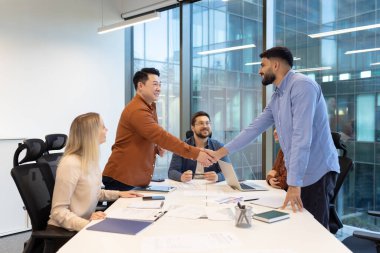 Bir grup profesyonel, modern bir ofis ortamında takım çalışmasını teşvik ederken, fikirleri tartışarak ortak bir toplantıya katıldı. İki meslektaş, profesyonel anlaşmayı simgeleyen el sıkışıyorlar.