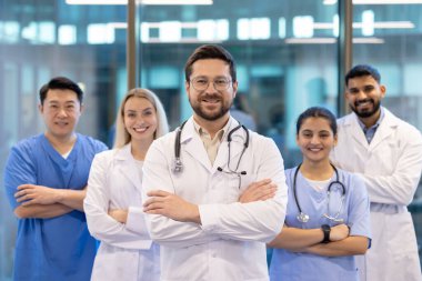 Çeşitli sağlık uzmanlarından oluşan bir ekip modern hastane ortamında güvenle gülümsüyor. Ekip çalışmalarının gösterilmesi ve hastalara kaliteli tıbbi bakım sağlanması ve güvenin artırılmasında kararlılık.