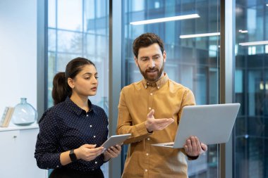 Modern bir ofis ortamındaki iki meslektaşı, canlı bir çalışma alanında takım çalışması, teknoloji entegrasyonu ve profesyonel işbirliğinin vurgulandığı bir dizüstü bilgisayar ve tablet kullanarak bir proje üzerinde işbirliği yapıyorlar.