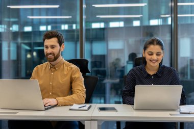 İki profesyonel çağdaş ofis ortamında dizüstü bilgisayarlar üzerinde birlikte çalışıyor. Görüntü, profesyonel bir ortamda takım çalışması, işbirliği, odaklanma ve verimliliği yansıtır.