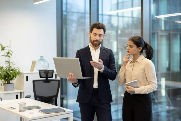 Two professionals collaborating in a well-lit contemporary workspace, focusing on a laptop computer while brainstorming ideas and strategies for their business project.