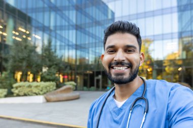 Önlük ve steteskop takan bir tıp uzmanı, binanın yakınlarında parlak bir şekilde gülümseyen, sağlık hizmetlerindeki olumlu, becerikli ve yaklaşılabilir davranışları aktaran biri..