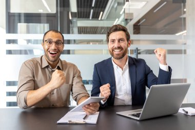 İki meslektaşından oluşan neşeli bir ekip modern ofis ortamında başarılarını kutlarken coşkuyla gülümsüyor..