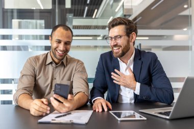 Modern bir ofiste iş birliği yapmak için akıllı telefon kullanırken sohbet eden iki meslektaşla canlı bir toplantı..
