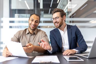 İki meslektaş bir ofiste iş belgeleri üzerinde işbirliği yapıyor. Gülümsüyorlar ve nişanlı görünüyorlar..