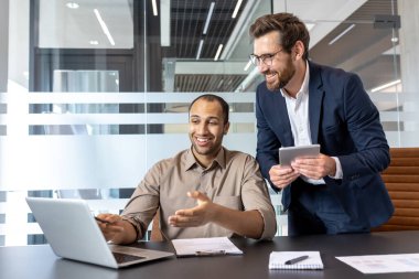 İki iş arkadaşı bir ofiste dizüstü bilgisayar ve tablet kullanarak fikirleri tartışır..