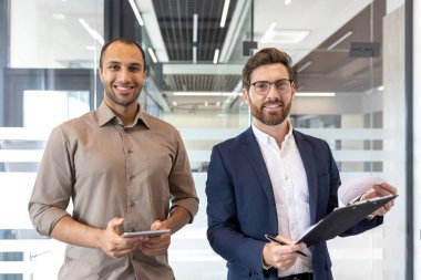 Profesyonel kıyafetli iki kişi bir iş görüşmesi için çağdaş bir ofiste buluşuyor. Pozitif ve görevlerine odaklanmış görünüyorlar..