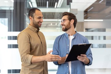Ofiste yan yana duran iki profesyonel gülümsemeli ve hareketli bir belgeyi tartışıyorlar..