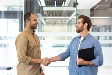 Çağdaş bir ofis içinde el sıkışan iki birey, takım çalışmasını ve ortaklığı yansıtıyor. Sahne, modern çevrede profesyonel bir etkileşim ve işbirliği içeriyor..